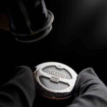 Technicien inspectant un fond de boîte Tissot avec une loupe, gants noirs et éclairage focalisé