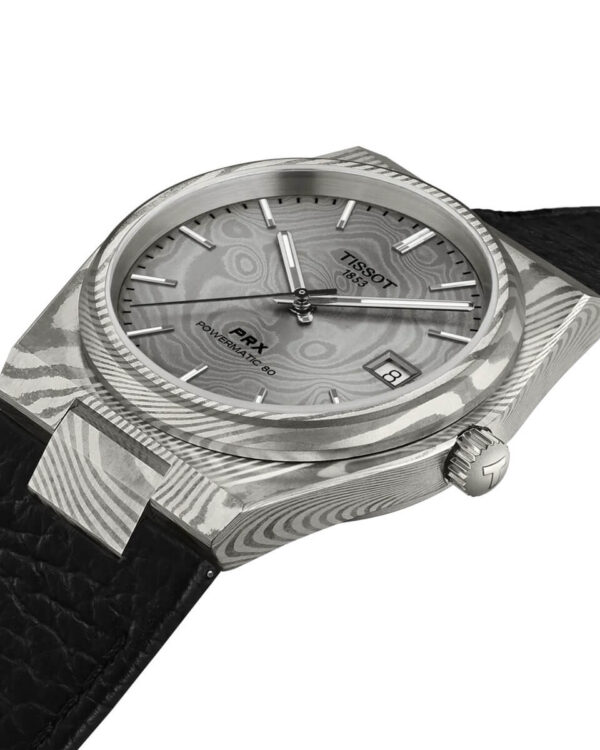 Gros plan sur la montre Tissot PRX Powermatic 80 Acier Damas, montrant le cadran gris et le boîtier marbré en acier damas avec bracelet en cuir noir.