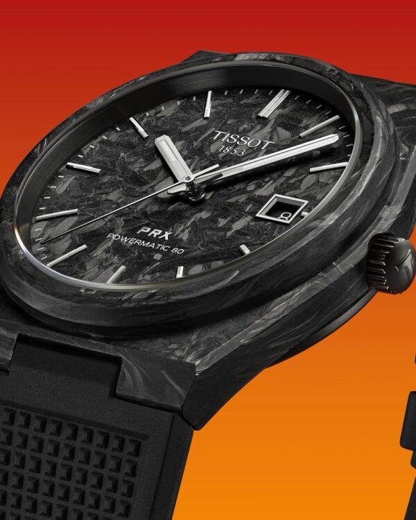 Gros plan sur la montre Tissot PRX Powermatic 80 Carbone, montrant le cadran noir texturé en fibre de carbone et le boîtier en composite noir sur fond dégradé orange.